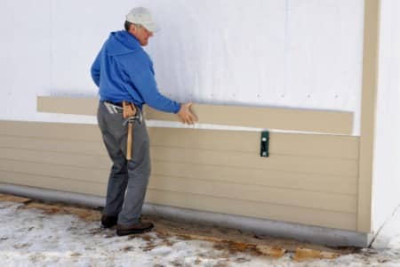 A worker professionally installing siding on a home
